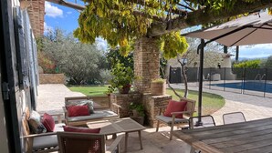 An outdoor patio with stone flooring, wooden furniture, and a pool in the background. - Large Provençal-style family home with swimming pool in a quiet location (Saint-Maximin-la-Sainte-Baume)