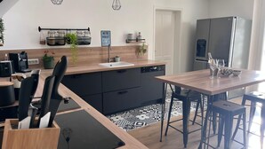 A modern kitchen with a wooden countertop, black cabinets, and a built-in dishwasher. There are hanging light fixtures, a coffee machine, and a refrigerator. - Large Provençal-style family home with swimming pool in a quiet location (Saint-Maximin-la-Sainte-Baume)