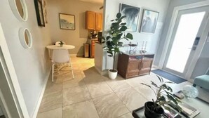 Una sala de estar moderna con comedor, una cocina al fondo y una planta grande en maceta.