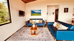 A living room with a blue sofa, a wooden coffee table, and a painting on the wall. - Lake Sunset House in Arenal-quiet retreat spectacular views (Tilaran)
