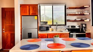 A modern kitchen with wooden cabinets, a stainless steel refrigerator, a microwave, a coffee maker, and a window with a view of greenery. - Lake Sunset House in Arenal-quiet retreat spectacular views (Tilaran)