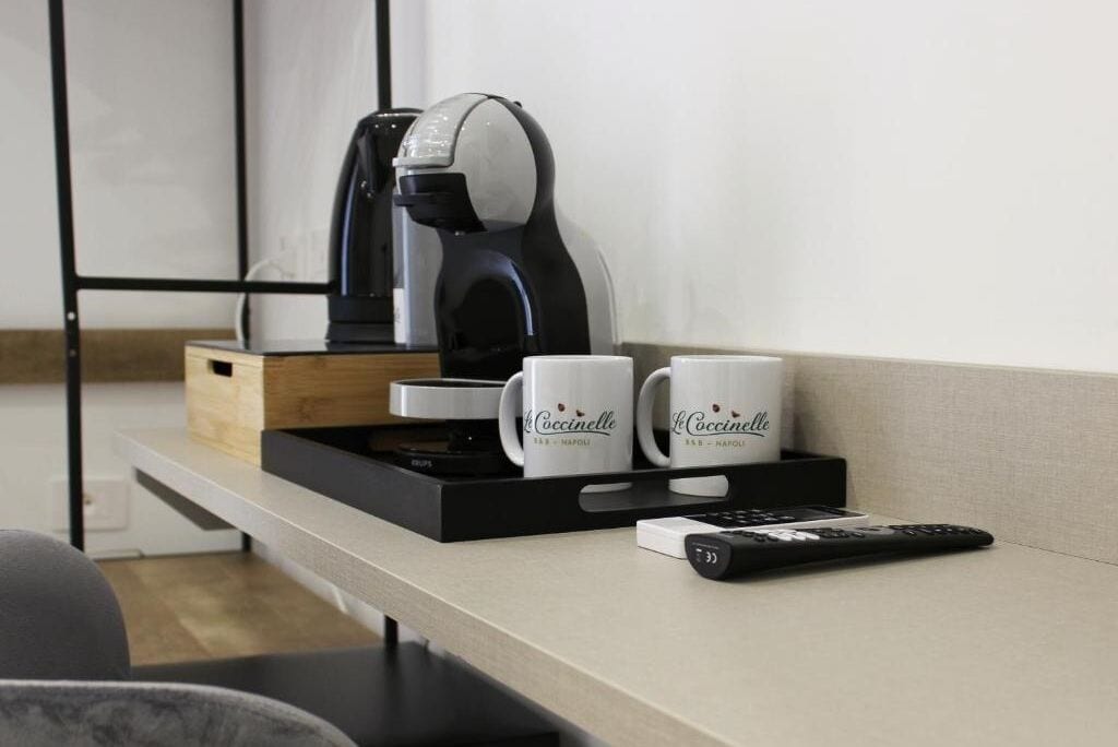 A coffee maker, two coffee mugs, and a remote control on a tray.
