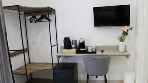 A compact room with a bed, a desk, a chair, a TV, a coffee maker, and a trash bin. - Cozy and equipped with amenities, for couples and families in a quiet setting. (Napoli)