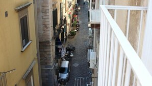 A narrow street with buildings on either side, a parked car, and a white railing in the foreground. - Cozy and equipped with amenities, for couples and families in a quiet setting. (Napoli)