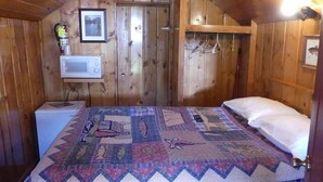 A wooden cabin bedroom with a quilted bedspread, a white microwave, and a framed picture on the wall. - Madison River Cabin Rental #2 (W YELLOWSTONE)