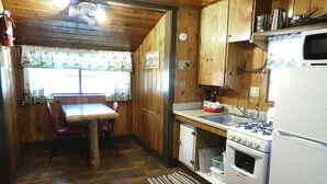Una cocina compacta con armarios de madera, estufa, fregadero y una mesa de comedor con sillas.