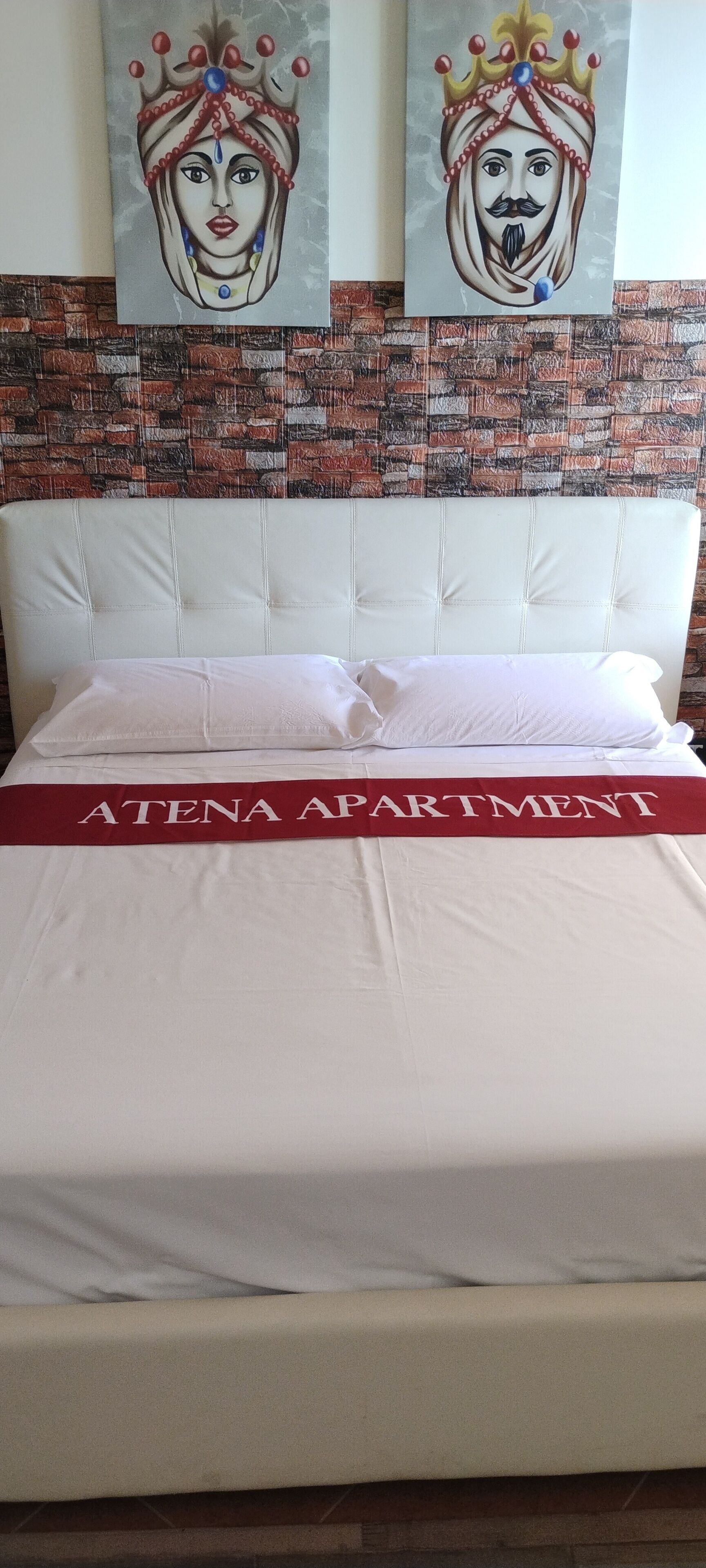 A bed with a white headboard and a red banner reading "ATENA APARTMENT".