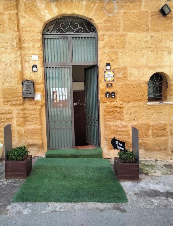 Un edificio de piedra con una entrada arqueada grande, un césped artificial verde y un cartel que indica '10th Avenue Apartments'.