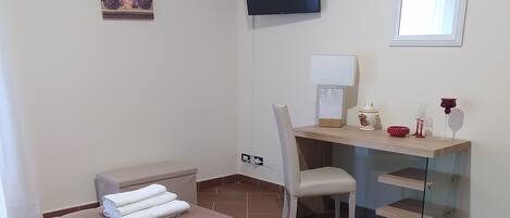 A hotel room with a bed, a desk, a chair, a TV, and a window.