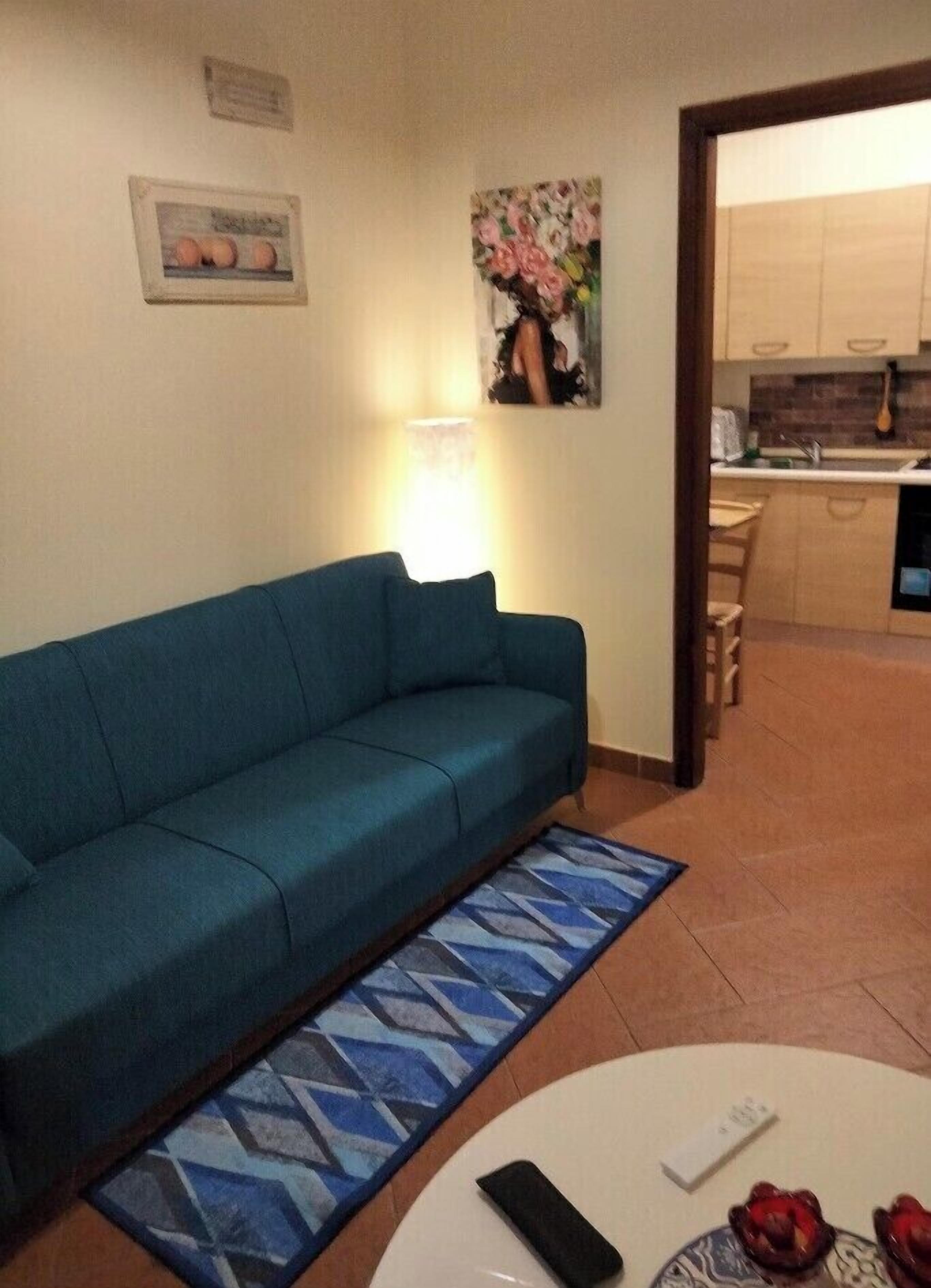 A living room with a teal sofa, a patterned rug, and a small white table with a remote control and fruit.