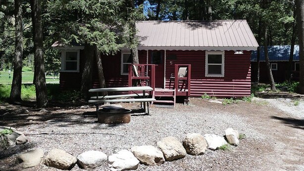 En enkel stuga med ett plåttak, en veranda med röda stolar och ett picknickbord.