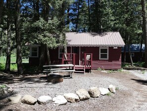 A rustic cabin with a metal roof, a porch with red chairs, and a picnic table. - Madison River Cabin Rental #5 (W YELLOWSTONE)