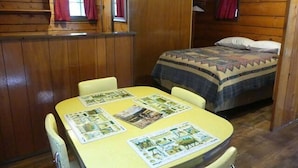 A cabin with a bed, a dining table with placemats, and wooden walls. - Madison River Cabin Rental #6 (W YELLOWSTONE)
