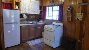 A compact kitchen with wooden walls, a refrigerator, a microwave, a stove, and a sink. - Madison River Cabin Rental #6 (W YELLOWSTONE)