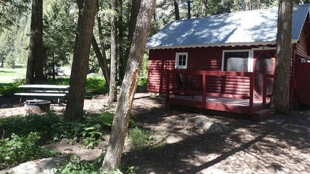A small red cabin with a porch, surrounded by trees. - Madison River Cabin Rental #6 (W YELLOWSTONE)
