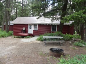 A rustic cabin with a metal roof, a wooden deck, and a picnic table. - Madison River Cabin Rental #7 (W YELLOWSTONE)