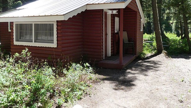 Eine kleine, eingeschossige Holzhütte mit Veranda, Fenster und Tür.