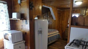 Ein gemütliches Holzhäuschen mit einer Küchenzeile, einem Bett mit gemustertem Überwurf und einem kleinen Kühlschrank.