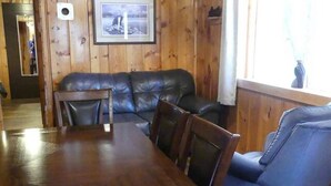 A wooden-paneled room with a leather sofa, a blue armchair, and a wooden dining table. - Madison River Cabin Rental #9 (W YELLOWSTONE)