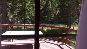 A wooden deck with a red railing overlooking a forested area. - Madison River Cabin Rental #12 (W YELLOWSTONE)