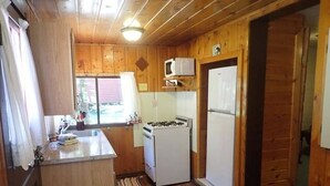 A compact kitchen with wooden walls, a refrigerator, a microwave, and a stove. - Madison River Cabin Rental #12 (W YELLOWSTONE)