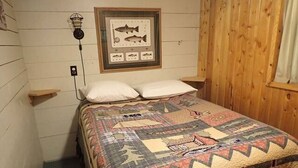 A small, cozy room with a bed, a framed fish illustration on the wall, and a small shelf. - Madison River Cabin Rental #12 (W YELLOWSTONE)