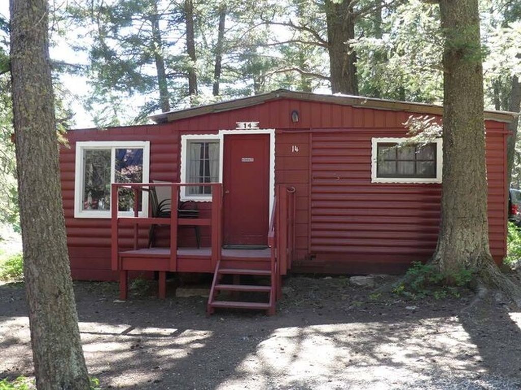 A red cabin with a small porch and a door, surrounded by trees.