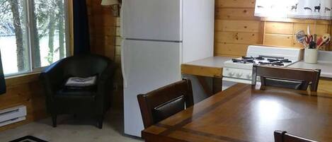 A wooden cabin kitchen with a refrigerator, stove, and dining table.