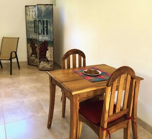 Een houten eettafel met een bord koekjes, twee houten stoelen en een poster aan de muur.