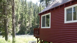 En rød hytte med terrasse, omgivet af skov.