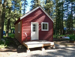 A small, single-story cabin with a red exterior and white trim, surrounded by trees. - Madison River Cabin Rental #22 (W YELLOWSTONE)