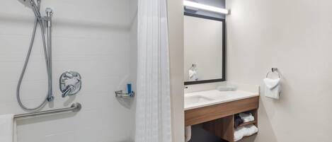 A modern bathroom with a shower, grab bar, and a vanity with a mirror.