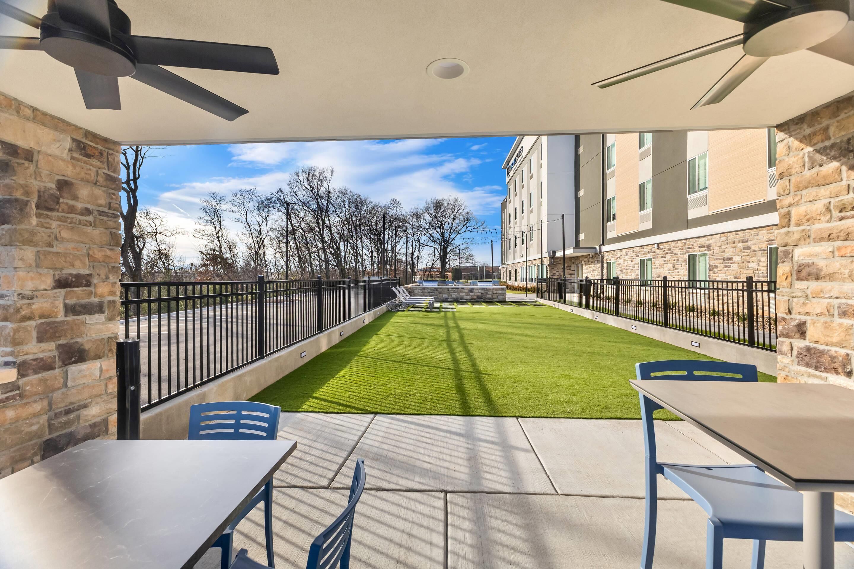 Een patio met een tafel en stoelen, een plafondventilator en uitzicht op een gebouw en bomen.