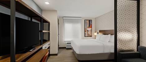 A hotel room with a bed, a TV, a desk, and a seating area.