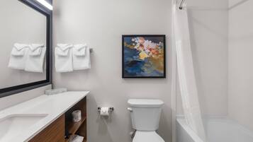 A bathroom with a toilet, a sink, a mirror, a shower, and a painting on the wall.