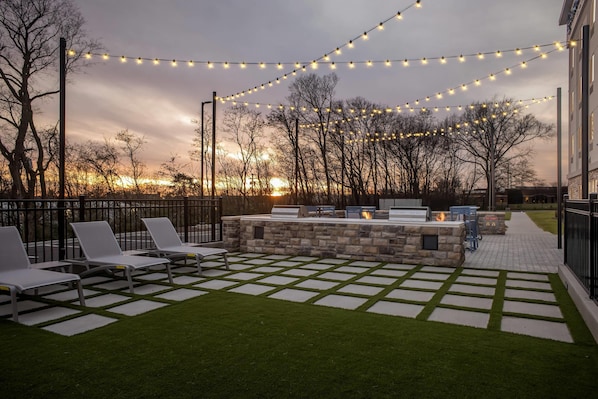 An outdoor seating area with a stone fire pit, lounge chairs, and string lights against a sunset backdrop. - Everhome Suites Clarksville Ft. Campbell Area by Choice Hotels (Clarksville)