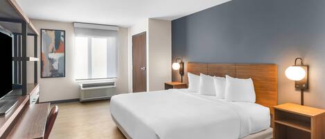 A modern hotel room with a large bed, wooden headboard, bedside tables with lamps, a desk, and a large window.