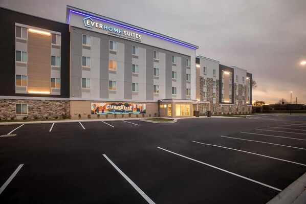A hotel with a modern facade, multiple floors, and a parking lot.