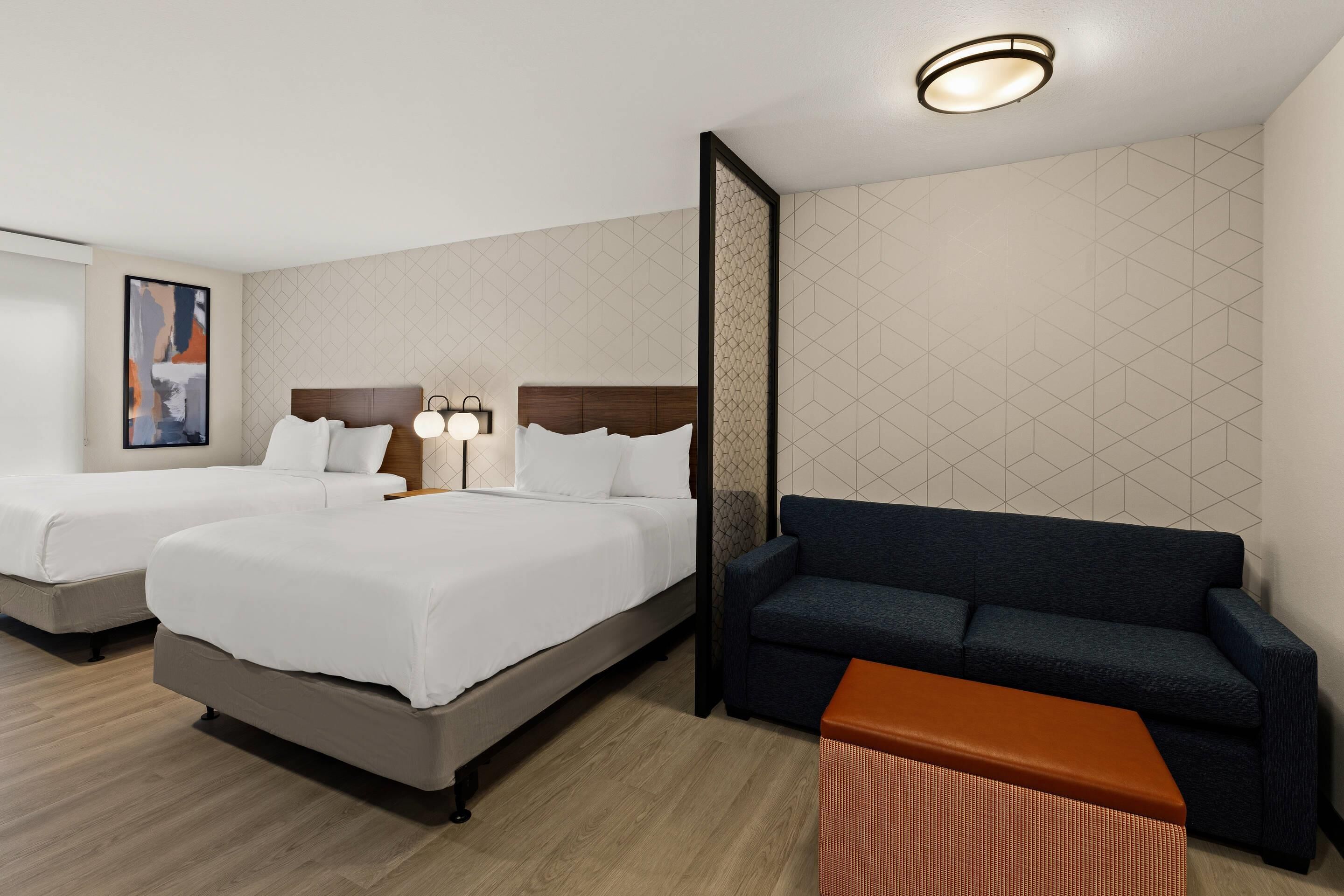 A hotel room with two beds, a sofa, a small table, and a wall with geometric patterns.