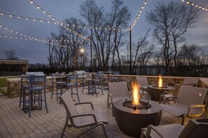 An outdoor patio with seating, a fire pit, and string lights.