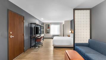 A hotel room with a wooden door, a desk with a computer, a bed, a blue sofa, and a patterned wall.