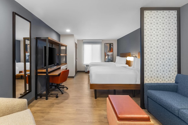 A modern hotel room with a large bed, a desk with a computer, a chair, a sofa, and a TV.