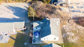 An aerial view of a residential property with a house, a fenced yard, and a sandy area with beach chairs.