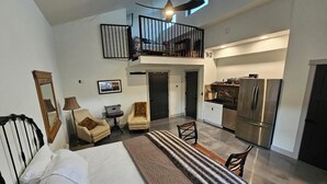 A modern hotel room with a large bed, a desk, a chair, a small table, and a balcony with a railing. - The 4-bedroom Brook House Barndominium is the perfect space for you! (Colorado Springs)