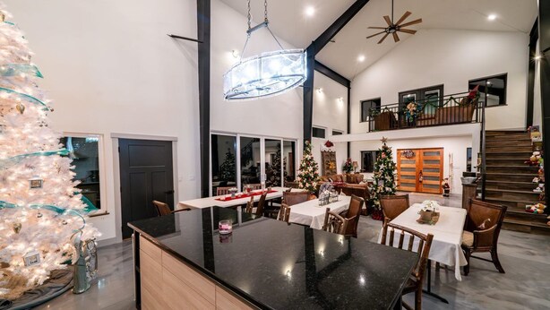 A spacious living area with a large island table, a Christmas tree, and a staircase leading to an upper level. - The 4-bedroom Brook House Barndominium is the perfect space for you! (Colorado Springs)