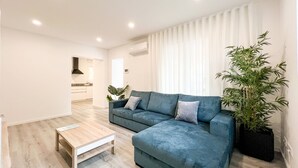 Un saló modern amb un sofà blau, una taula de centre de fusta i una planta gran en test.