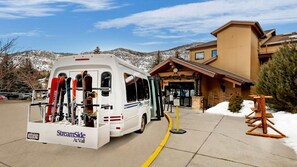 A ski resort with a shuttle bus, snow-covered mountains, and a lodge with a wooden facade. - Vail Loft – StreamSide Douglas Retreat Near Skiing, Creek & Village (Vail)