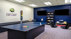 Ein Zimmer mit Tischtennisplatte, Bücherregal, Fernseher und einer Wand mit Sternenmuster.