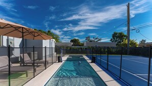 Une piscine dotée d’une zone délimitée par un filet, de chaises longues et d’un espace de repos abrité.