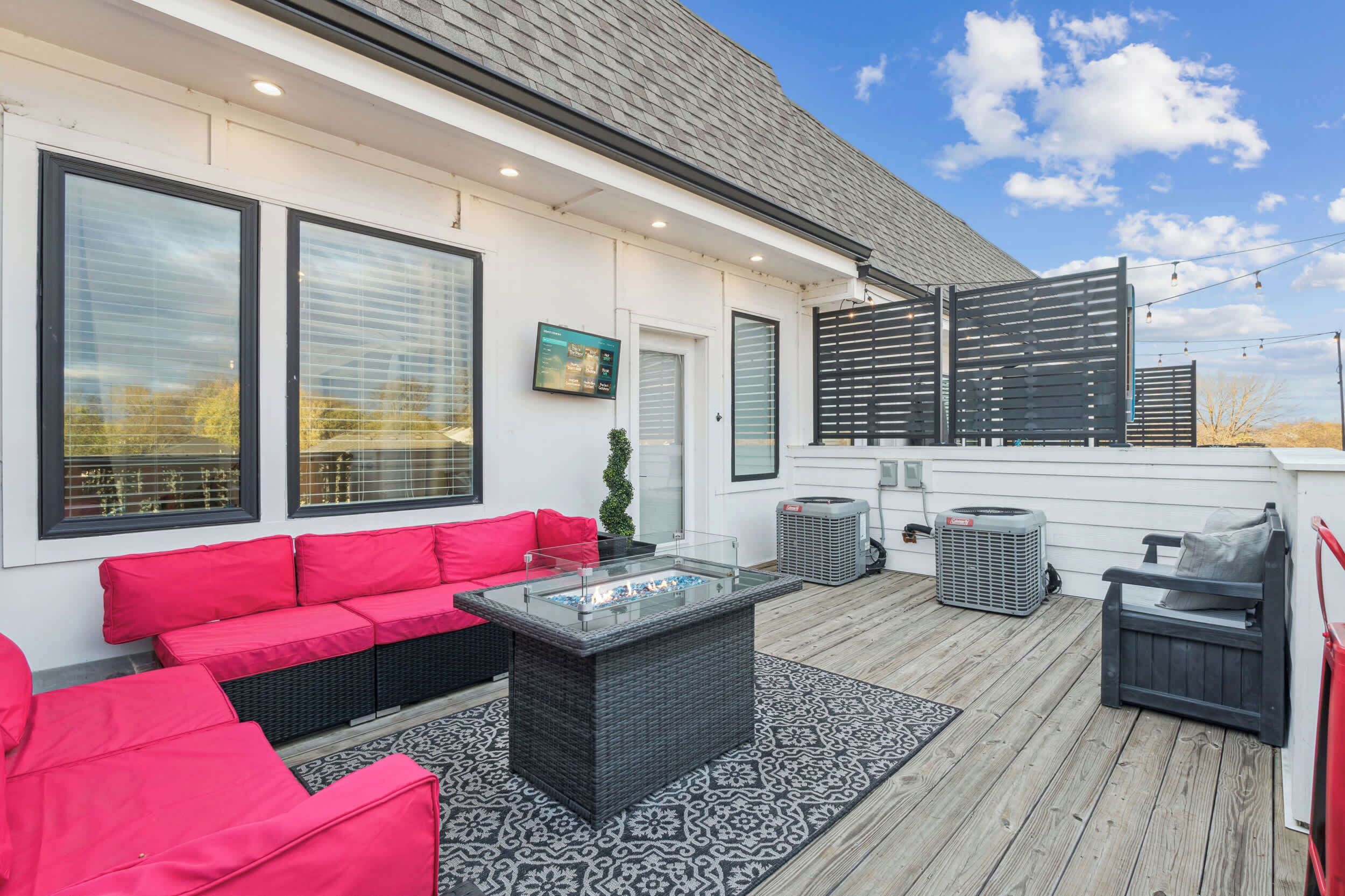 An outdoor patio with a glass-top table, red and black wicker furniture, and a gray air conditioning unit.